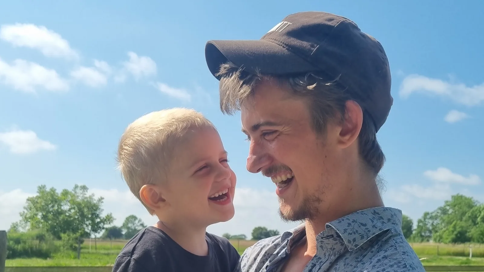 Filip med sin søn på armen i en grøn mark — de griner og kigger på hinanden.